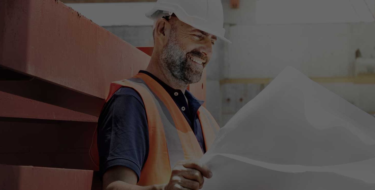 Smiling contractor in a hard hat reviewing plans on a job site